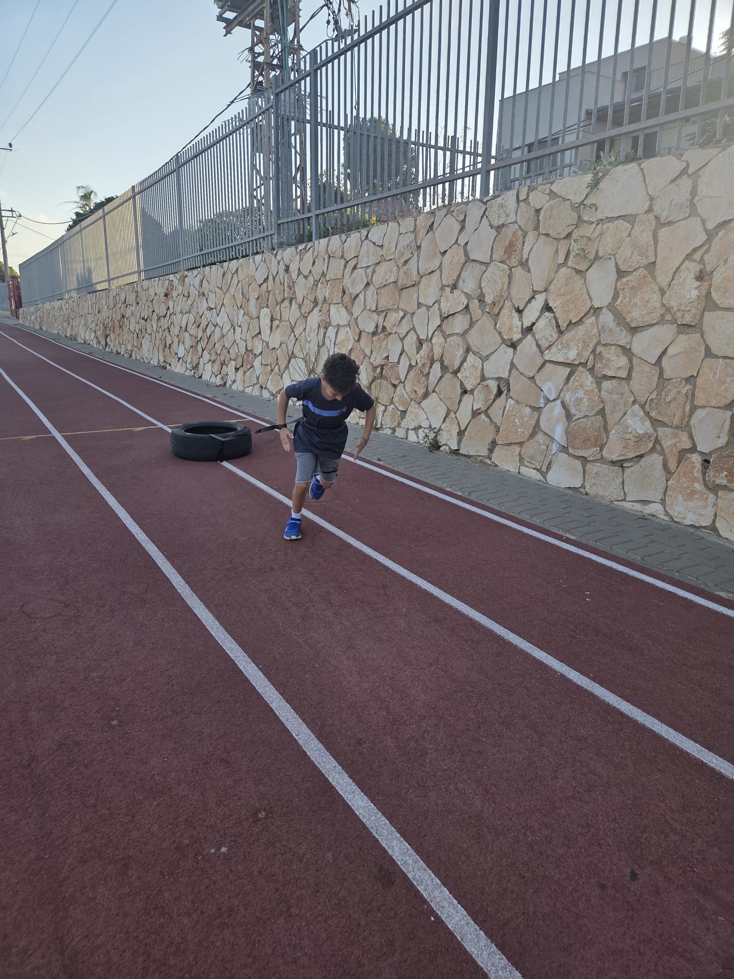 נער מתאמן על כוח מתפרץ בגרירת צמיג על מסלול אתלטיקה